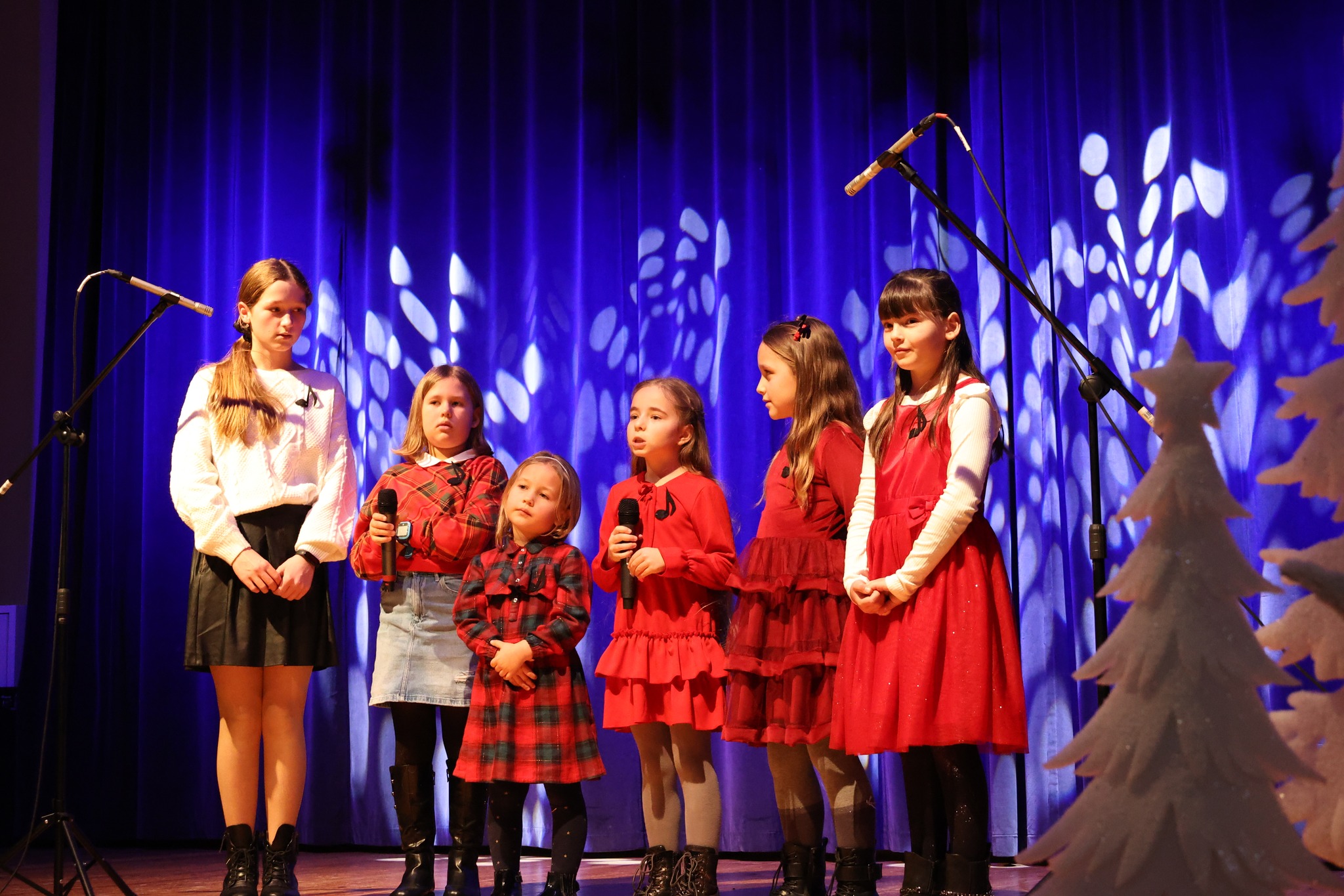 Sześć dziewczynek w świątecznych strojach stojących na scenie, niebieskie tło